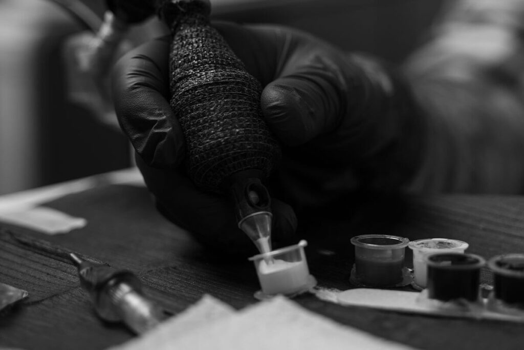 Tattoo artist dipping machine into white ink cap